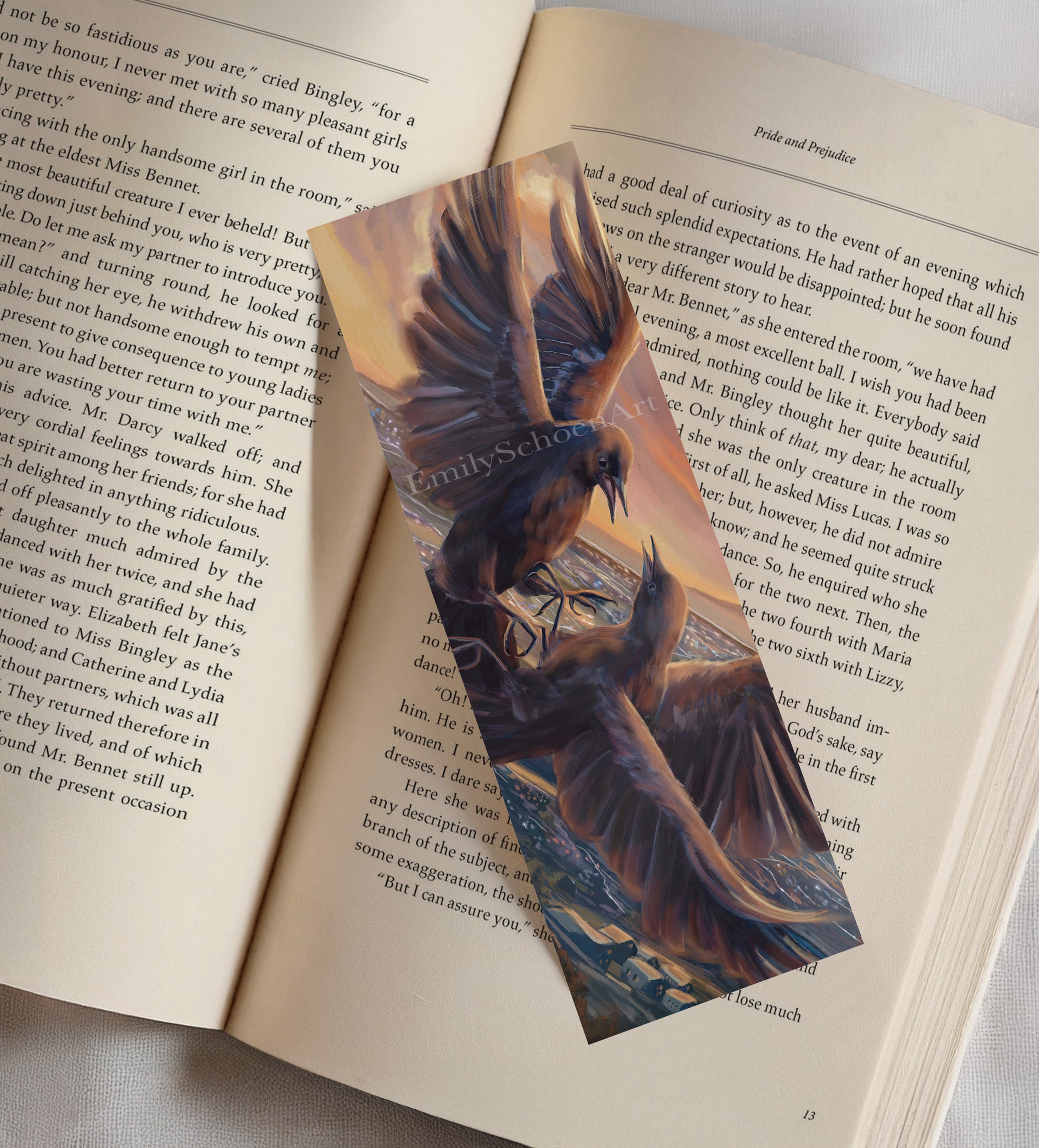 A bookmark on top of an open book with artistic depiction of two birds in flight facing each other against a sunset and over a city