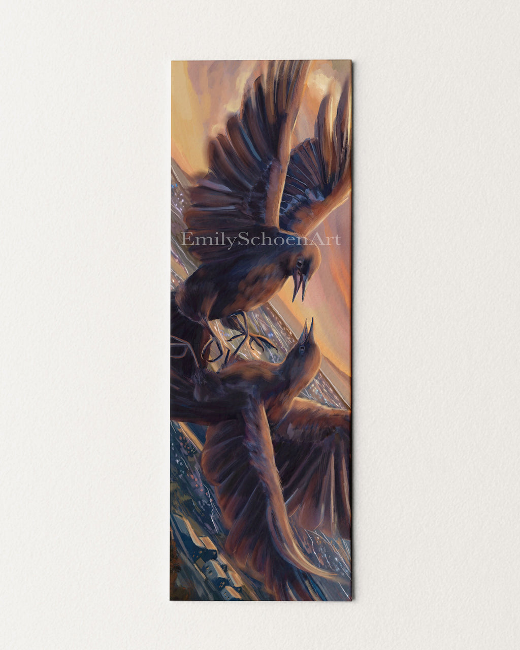 A bookmark with artistic depiction of two birds in flight facing each other against a sunset and over a city